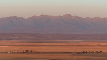 Obraz premium A vast grassland stretches to the horizon with majestic mountains in the backdrop,