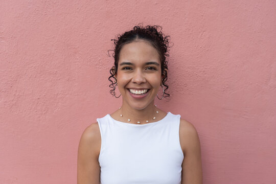 Young latin woman smiling over pink background