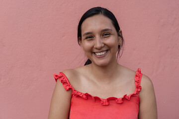 Young latin woman smiling by pink wall