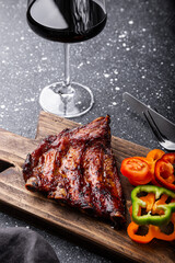 BBQ pork ribs from pork tenderloin with vegetables, ketchup and a glass of red wine on dark background vertical photo