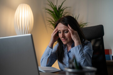 Stressed businesswoman working late on laptop in office, fatigue and overwork concept in...
