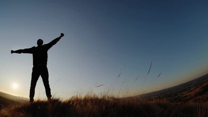 Feeling victorious while standing on the hilltop at sunset in an open field