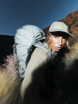 Image of a girl wearing a cap with a hiking backpack, with wildflowers sticking out. Hiking and mountain trekking. Motion blur.