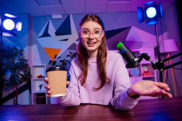 Young female blogger recording a podcast with microphone, coffee cup, and creative background in...