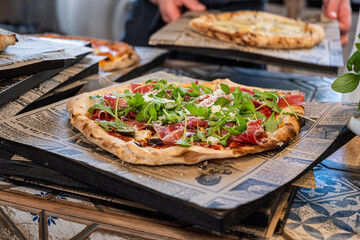 Fresh homemade pizza topped with crispy prosciutto and vibrant arugula, served on rustic wooden boards in a cozy restaurant setting, perfect for food lovers