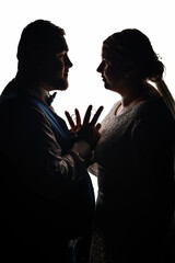 Silhouette of a bride and groom facing each other, holding hands with wedding rings between their fingers, creating a romantic and artistic wedding moment.