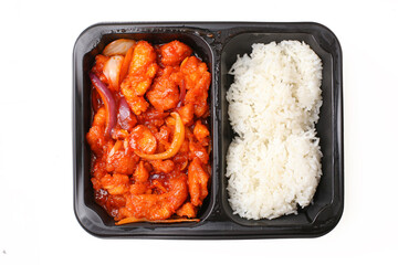 Takeaway meal box with sweet and sour chicken and white rice isolated on white background. Asian food delivery in black plastic container. Ready meal portion. Fast food concept closeup view.