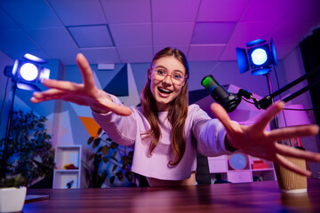 Confident young woman hosting a live podcast in a vibrant studio with neon lights and a professional microphone setup
