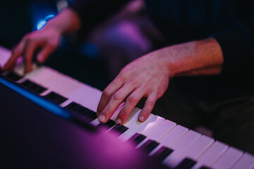 Obraz premium A detailed view of a person's hands gracefully playing the piano in a dimly lit room, conveying emotion and expertise. The ambient lighting adds drama and focus to the musical performance.