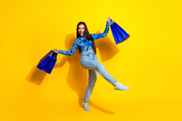 Smiling woman holding shopping bags and posing stylishly against a bright yellow background,...