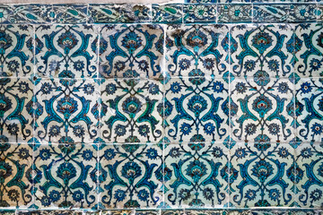 Traditional Islamic ceramic tile wall decorated with blue and turquoise arabesque floral motifs, ornamental detail from Middle Eastern architecture.