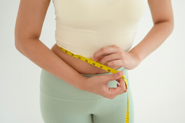 Young asian woman holding measuring tape checking her body after yoga exercise