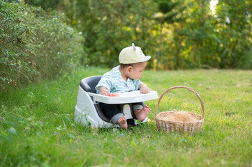 Baby Sitting in a High Chair on a Sunny Day in a Green Garden Enjoying Colorful Toys and a Basket