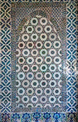 Traditional Islamic ceramic tile wall featuring geometric and floral motifs in blue and green colors, ornamental detail from Middle Eastern architecture