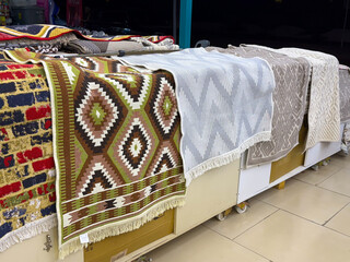 Row of patterned rugs displayed in a market with diverse geometric designs. Tradition, craft and...