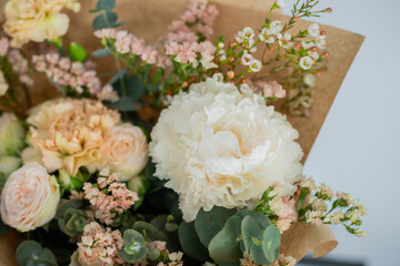 Delicate bouquet of flowers in light shades packed in craft paper close-up. European flower arrangement of white peony, pink spray roses, chamelacium, eucalyptus and yellow carnations.