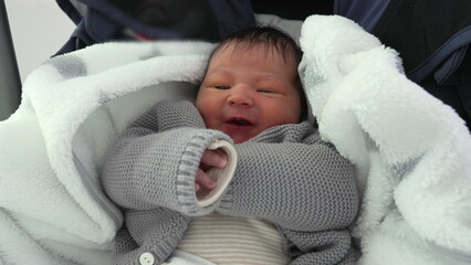 Newborn baby bundled in a cozy blanket and warm clothing, showing a slight frown, capturing a...