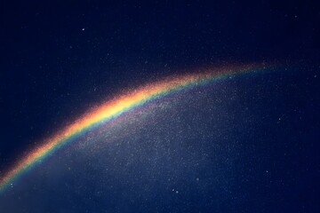 Fototapeta premium A single, vibrant rainbow is seen in the sky at night, casting its colors across an endless expanse of dark blue space.