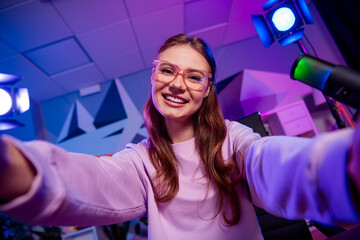 Young woman in casual stylish outfit streaming a podcast with vibrant neon studio lights featuring...