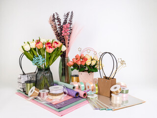 Still life of a set for florists, vases with artificial flowers, paper with flowerpots, multi-colored ribbons and dried flowers on a white background