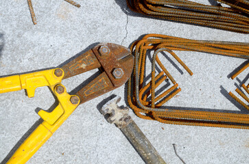 A top-down view of rusty bolt cutters and bent rebar on a gray concrete background. This image...