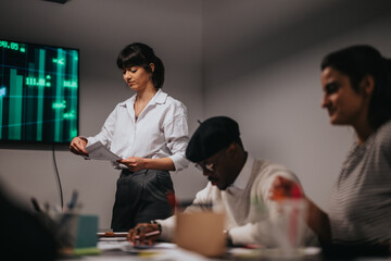 Team members collaborate during a business meeting, with a leader discussing data on a display...