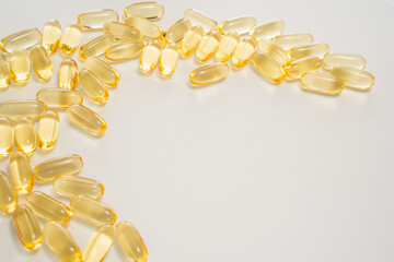 Numerous yellow gel capsules scattered across a clean white surface represent dietary supplements...