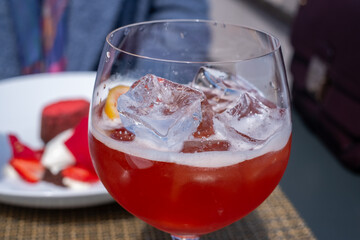 Refreshing cocktail in a large glass filled with ice cubes, vibrant red liquid, garnished with a...