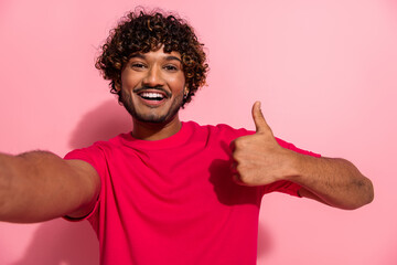 Smiling young man gesturing thumbs up in casual red shirt against a pink backdrop highlighting his cheerful personality
