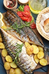 Tasty roasted mackerels served with spices and vegetables on blue wooden table, flat lay. Homemade seafood dish