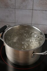 Metal pot with boiling water on stove in kitchen, closeup