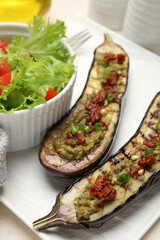 Slices of grilled eggplant with sun dried tomatoes, pesto and salad on white table, closeup