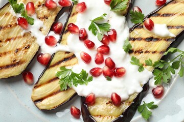 Slices of grilled eggplant with pomegranate seeds and yoghurt on table