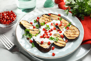 Slices of grilled eggplant with pomegranate seeds and yoghurt on white marble table, closeup