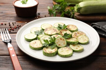 Delicious fried courgette slices with parsley served on wooden table, closeup