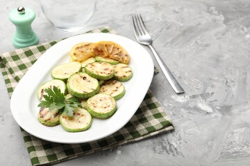 Delicious fried courgette slices with lemon and parsley served on grey table, closeup. Space for text