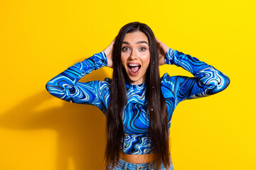 Cheerful young woman with long hair in a vibrant blue patterned top posing against a yellow...