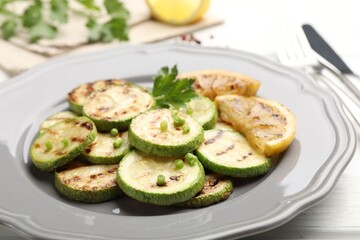 Delicious fried courgette slices with lemon, green onion and parsley on white wooden table, closeup