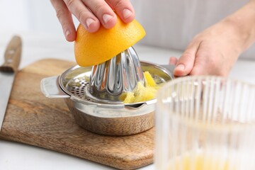 Making juice. Woman with orange using juicer at white table indoors, closeup