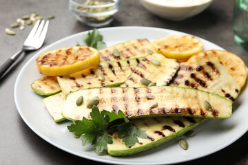 Delicious grilled courgette slices with pumpkin seeds, lemon and parsley on grey table, closeup