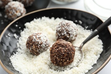 Making tasty chocolate candies with nuts and coconut flakes at white table, closeup