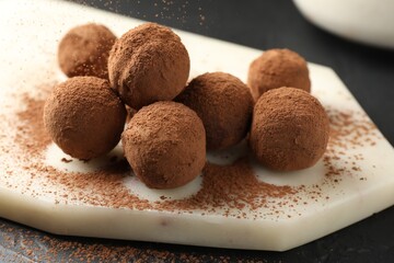 Tasty chocolate candies with cocoa powder on black table, closeup