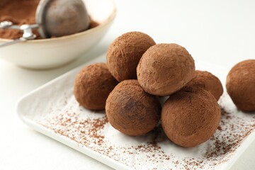 Tasty chocolate candies with cocoa powder on white table, closeup