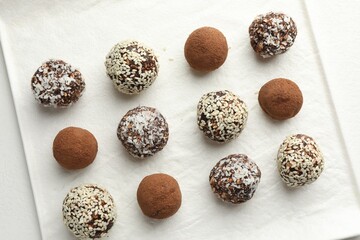 Tasty chocolate candies with cocoa powder, nuts and sesame seeds on white table, top view