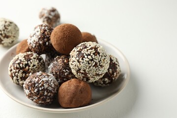 Tasty chocolate candies with cocoa powder, nuts and sesame seeds on white table, closeup. Space for text