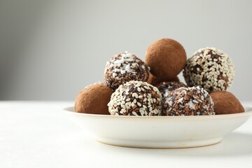 Tasty chocolate candies with cocoa powder, nuts and sesame seeds on white table, closeup