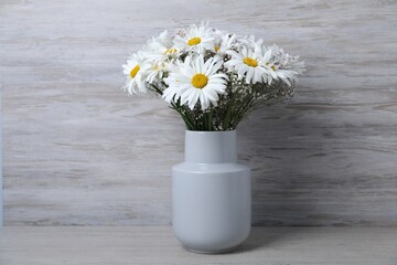 Beautiful chamomile and gypsophila flowers in vase on grey wooden table