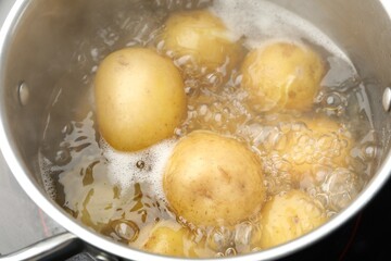 Young potatoes boiling in pot on stove, closeup