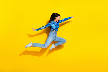 Energetic young woman jumping in stylish blue top on vibrant yellow background capturing energy and...