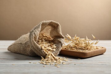 Oat flakes, sack and spikes on light wooden table against beige background, closeup